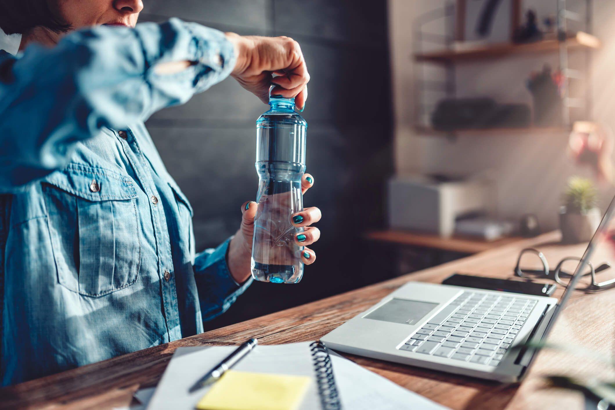 Person opening a water bottle in front of laptop